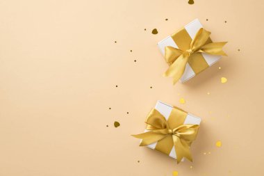Top view photo of valentine's day decorations two white gift boxes with golden silk ribbon bows sequins and heart shaped confetti on isolated beige background with blank space