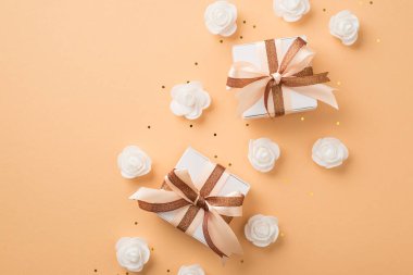 Top view photo of valentine's day decor white gift boxes with glowing brown and light beige ribbon bows white decorative roses and golden sequins on isolated beige background with copyspace