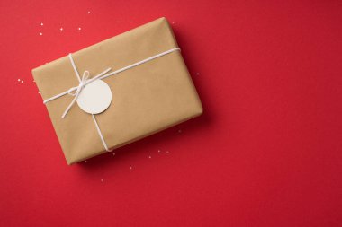 Top view photo of saint valentine's day decorations sequins craft paper giftbox with bow and pricetag on isolated red background with empty space