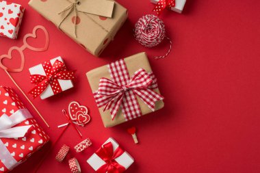Top view photo of saint valentine's day decorations handicraft tools spool of twine heart shaped glasses tape clothespins and gift boxes on isolated red background with copyspace