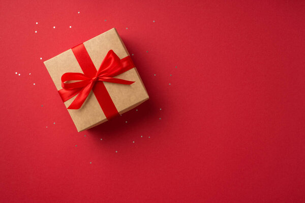 Top view photo of saint valentine's day decorations glowing sequins and craft paper giftbox with red ribbon bow on isolated red background with copyspace