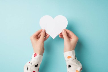 Sevgililer günü dekorasyonunun birinci şahıs fotoğrafı beyaz tişörtlü bir kızın elleri, izole edilmiş pastel mavi arka planda beyaz kağıt kalp ve boş bir alan.