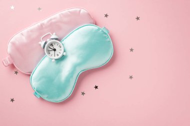 Üst görüntüde pembe ipek uyku maskesi bulutları ve izole edilmiş pastel pembe arka planda altın yıldızlar kopyalanmış.