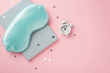 Mavi ipek uyku maskesinin üst görüntüsü küçük beyaz alarm saati hapları mavi hatırlatıcı ve izole edilmiş pastel pembe arka planda yıldız şekilli konfeti boş alan
