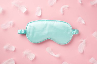 Açık mavi ipek uyku maskesi ve izole edilmiş pastel pembe arka planda pembe tüylü boş alan fotoğrafı.