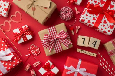 Sevgililer Günü dekorasyonunun en üst görüntüsü el işi aletleri sicim kalp şeklindeki cam bant çamaşır mandalları ahşap takvim kamışları ve izole edilmiş kırmızı arka planda hediye kutuları.