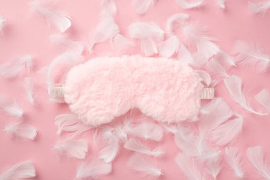 Üst görüntüde pembe tüylü uyku maskesi ve izole edilmiş pastel pembe arkaplandaki tüyler var.