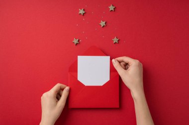 Sevgililer Günü dekorasyonunun birinci şahıs fotoğrafı. Kırmızı zarf yıldızlarından mektup alan kadın elleri ve kopyalanmış kırmızı zemin üzerindeki pullar.