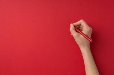 Sevgililer Günü dekorasyonunun birinci şahıs fotoğrafı. Kırmızı kalemi boş arkaplanda tutan kadın eli.