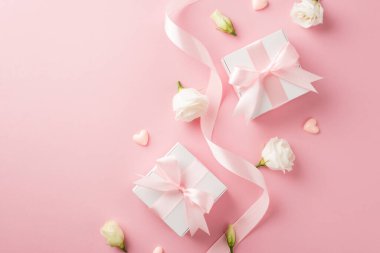 Kadınlar Günü 'nün en iyi görüntüsü beyaz hediye kutuları pembe fiyonklu kıvrık ipek kurdele küçük kalpler ve izole edilmiş pastel pembe arka planda beyaz çayır çiçeği tomurcukları.