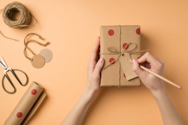 Üstten kadınların etikete yazı yazarken çekilmiş ilk fotoğraf. Kağıt hediye kutusuna polka desenli makas sarmalı, sicim izole edilmiş bej arkaplan.