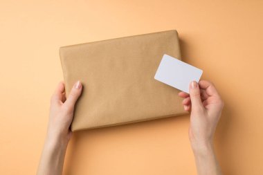 Üstten bakıldığında, genç bir kadının el işi kağıt hediye kutusu ve kartvizitle çekilmiş resmi kopyalanmış bej arka planda.