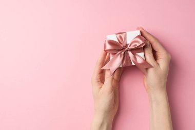 Sevgililer Günü dekorasyonunun birinci şahıs fotoğrafı. Küçük beyaz hediye kutusu, pembe kurdeleli, kopyalanmış pastel pembe arka planda.