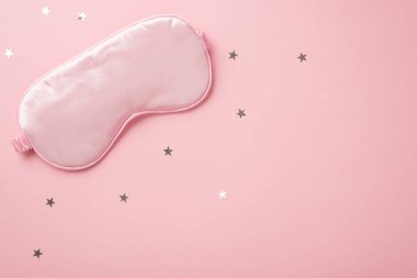 Pembe ipek uyku maskesi ve yıldız şekilli konfetilerin üst görüntüsü izole edilmiş pastel pembe arkaplanlı ve kopyalanmış