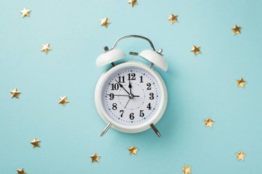 Pastel mavi arka plandaki büyük beyaz alarmın en üst görüntüsü. Altın yıldız şeklinde bir sürü dağınık konfeti.