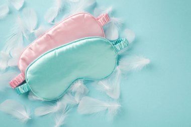 Pastel gökyüzüne saçılmış beyaz ışık tüyleri üzerinde iki büyük pembe ve mavi ipek göz bağı fotoğrafı.