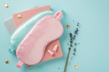 Mavi ve pembe saten uyku maskelerinin üst görüntüsü kulak tıkaçları altın yıldızları ve izole edilmiş pastel mavi arka planda lavanta filizi boş alan
