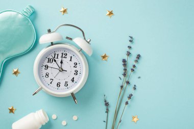 Lavanta mavisi ipek uyku maskesinden oluşan beyaz alarm saat filizinin en üstteki fotoğrafı. İçinde haplar ve izole edilmiş mavi arka planda altın yıldızlar bulunan uyku maskesi.