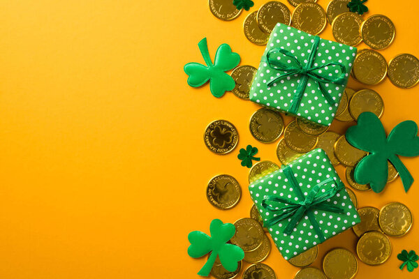 Top view photo of st patrick's day decorations two green gift boxes with polka dot pattern shamrocks clover shaped confetti and a lot of gold coins on isolated yellow background with empty space