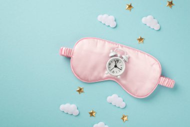 Pembe saten maske bulutları üzerinde beyaz alarmlı saatin ve izole edilmiş mavi arka planda altın yıldızların resmi.
