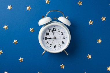 Beyaz, büyük saatin en üstteki fotoğrafı. Dağınık, mavi arka planda yıldız şeklinde altın bir konfeti.