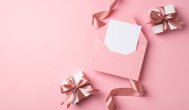 Sevgililer Günü dekorunun en üst görüntüsü pembe fiyonklu iki beyaz hediye kutusu ve izole edilmiş pastel pembe arka planlı kağıt kapaklı pembe bir zarf.