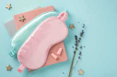 Mavi ve pembe ipek uyku maskelerinin üstteki fotoğrafı defterlerdeki kulak tıkaçları parlayan yıldızlar ve izole edilmiş pastel mavi arka plandaki lavanta filizi boş alan