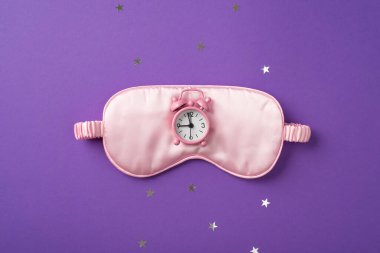 Büyük ipek göz bağı ve üzerinde menekşe arkaplanındaki yıldız şeklinde dağınık konfeti bulunan küçük pembe saatin en iyi görüntü fotoğrafı.