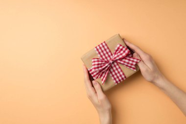 Sevgililer Günü dekorasyonunun birinci şahıs fotoğrafı. Bir kadın el sanatları hediye kutusu veriyor. Arkaplanda kareli kurdele var.