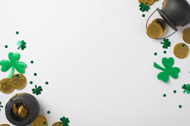 Yeşil konfetilerin içinde ve çevresinde altın sikkeler olan iki siyah kazanın üst görüntüsü farklı boyutlarda ve yonca şeklinde gölgeler ve beyaz izole edilmiş boş arkaplanda küçük noktalar.