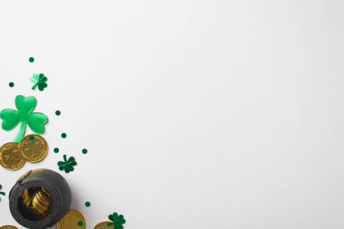 Yeşil konfetilerin içinde ve çevresinde altın sikkeler olan siyah bir kazanın en üstteki fotoğrafı. Farklı boyutlarda ve yonca ve noktalar şeklinde beyaz izole edilmiş arka plan boşluğunda.
