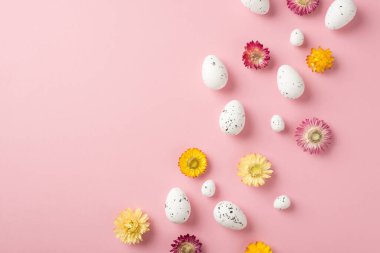 Paskalya süslerinin üst görüntüsü yabani çiçekler ve izole edilmiş pastel pembe arka planda beyaz paskalya yumurtaları.
