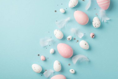 Paskalya süslemelerinin en üst görüntüsü tüyler pembe ve beyaz paskalya yumurtaları izole edilmiş pastel mavi arka planda kopyalanmış