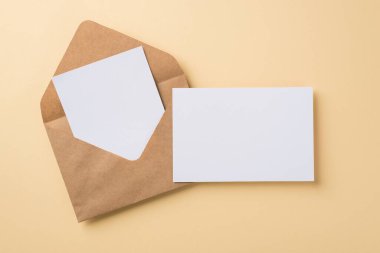 Bej izole edilmiş arka plan boşluğuna yerleştirilmiş iki beyaz kartpostallı büyük kahverengi el işi zarfının üst görünümü