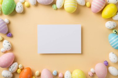Renkli pastel, orta ve küçük yumurtaların üst görüntüsü izole edilmiş bej arka planda ve ortasında boş kartpostal ile