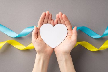 Ukrayna 'daki savaşı durdurun. Gri arka planda ulusal bayrak üzerinde avuçlarında beyaz kalbi tutan bir kızın el fotoğrafı.