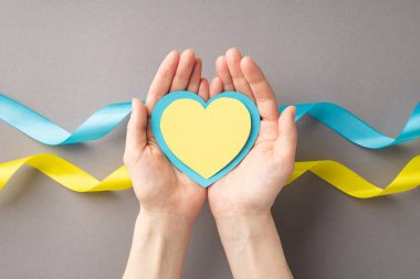 Ukrayna 'daki savaşı durdurun. Gri arkaplan üzerinde ulusal bayrak üzerinde mavi ve sarı kalp taşıyan bir kızın ellerinin resmi.