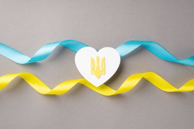 Ukrayna 'daki savaşı durdurun. Ulusal bayrak üzerinde altın mızraklı beyaz kalbin üst görüntüsü. İzole edilmiş gri arka planda mavi ve sarı dalgalı kurdeleler.