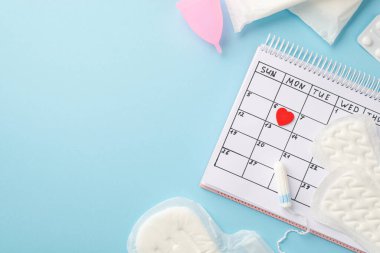 Takvimdeki kırmızı kalp işaretinin üst görüntüsü hijyenik peçeteler regl hapı ve izole edilmiş pastel mavi arka planda bulunan tampon.