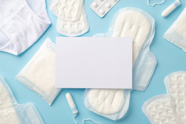 Hijyenik pedlerin, tamponların, ağrı kesicilerin, izole edilmiş pastel mavi arka planda, boş alanda çekilmiş kağıt tabloların en üstteki fotoğrafı.