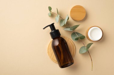 Doğal kozmetik konsepti. Cam şişe krem kavanozunun en üst görüntüsü okaliptüs ve izole edilmiş bej arka planda ahşap tezgah.