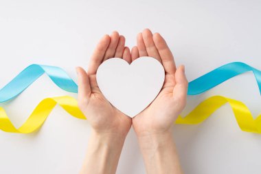 Ukrayna 'daki savaşı durdurun. Beyaz arka planda ulusal bayrak üzerinde avuçlarında beyaz kalbi tutan kadınların üst tepeden çekilmiş fotoğrafları.