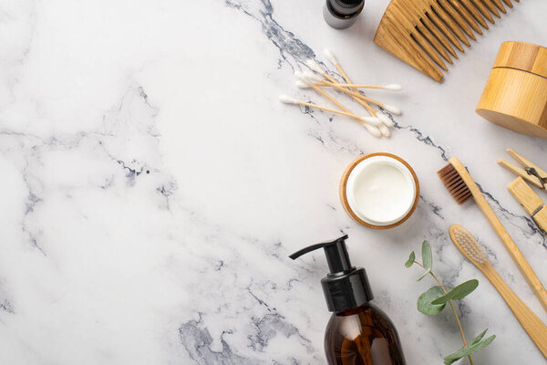 Фото верхнего вида стеклянных бутылок деревянная щетка крем для волос крем для волос зубные щетки ватные бутоны прищепки и эвкалипт на белом мраморном фоне с копипространством