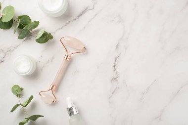 Cilt kozmetik konsepti. Beyaz mermer zemin üzerinde gül kuvars krem kavanoz cam şişe ve okaliptüs fotoğraf kopyalanmış