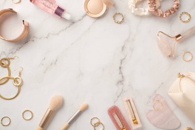 Pembe tokaların, gül kuvars roller gua sha şişe göz farı saç bandı altın küpe bileklik ve kozmetik çanta beyaz mermer arka planda ve ortadaki kopya alan.