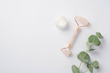 Cilt bakımı. Okaliptüs şube krem şişesinin ve kopyalanmış beyaz arka planda gül kuvars silindirinin üst görünümü