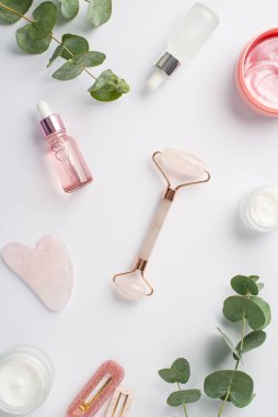 Rose Quartz 'ın dikey fotoğrafı gua sha pembe göz bantları kozmetik tokalarla şişeler ve izole edilmiş beyaz arka planda okaliptüs