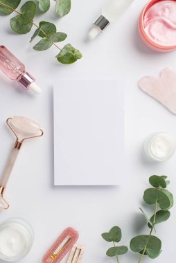 Üst görünüm kağıt çarşaf dikey fotoğraf kuvars gua sha pembe göz bantları cam şişeler saç tokaları ve okaliptüs izole beyaz arka plan boş alan