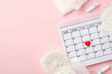 Takvimdeki kırmızı kalp işaretinin üst görüntüsü hijyenik peçeteler ve tamponlar izole edilmiş pastel pembe arka planda kopyalanmış