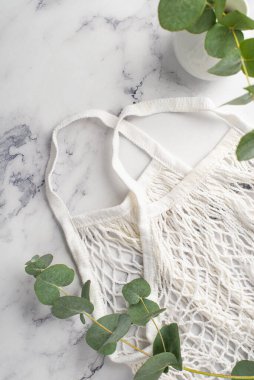 Çevre dostu kavram. Beyaz iplik torbası ve vazonun beyaz mermer zemin üzerinde okaliptüs ile üst görünüm dikey fotoğrafı